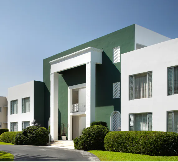 un bâtiment vert et blanc avec des buissons et des arbres